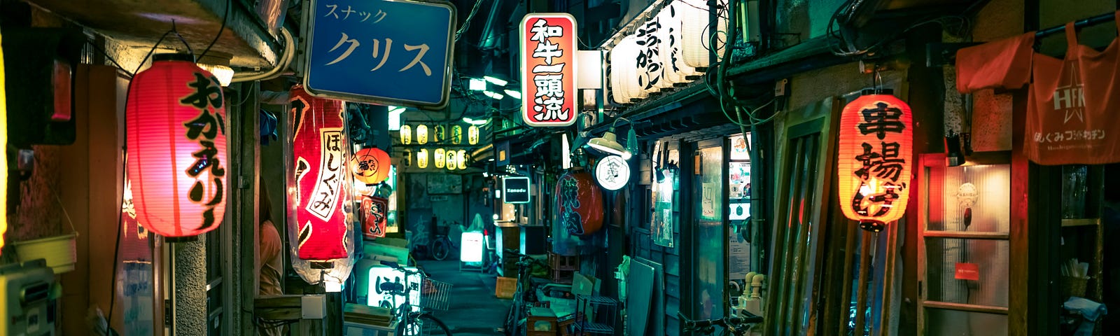 A Japanese alley full of restaurants and shops at night. The street is full of lanterns and neon lights.