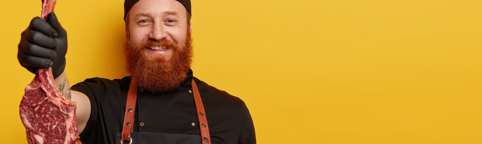 Bearded barbeque dude proudly holds up a raw steak.