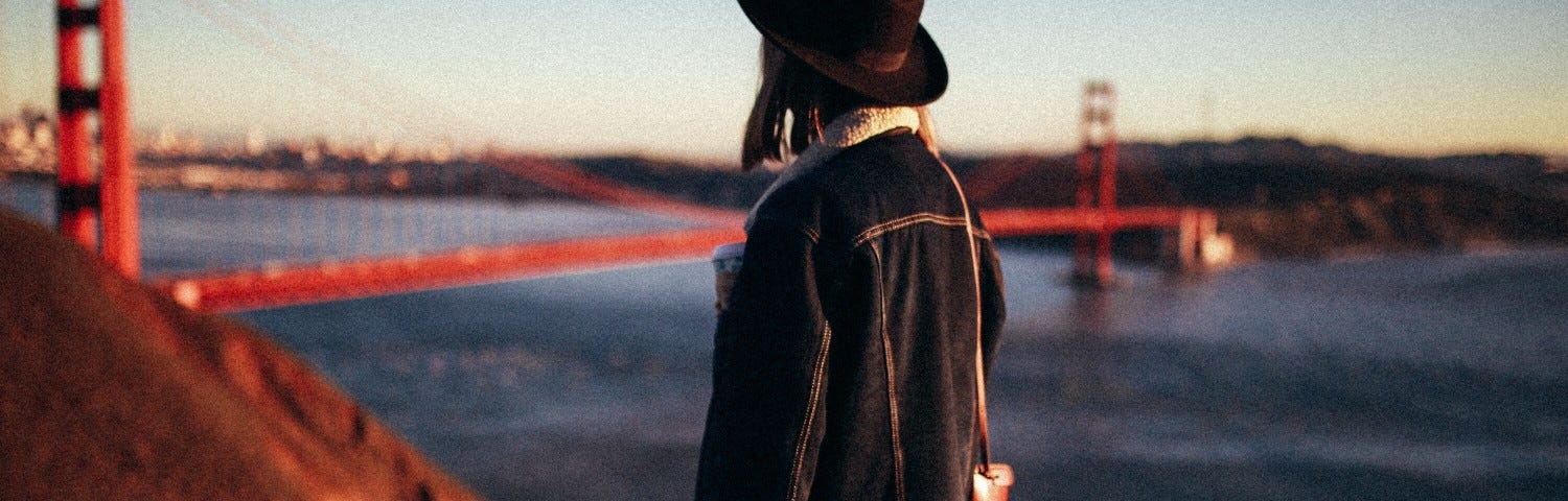 A woman stands facing the Golden Gate Bridge and San Francisco Bay.