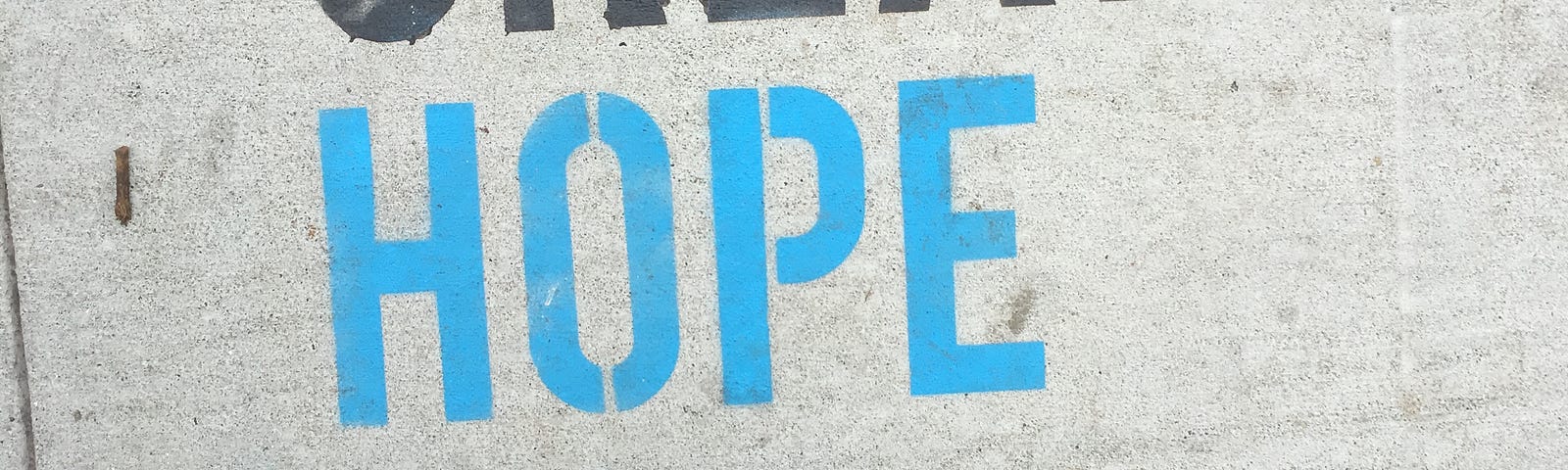 The words CREATE HOPE stenciled on a San Francisco sidewalk. The photographer (Dorothy) is wearing a pair of black platform boots, dark jeans, and a long blue sweater jacket. CREATE is spray painted in black and HOPE is painted in baby blue.