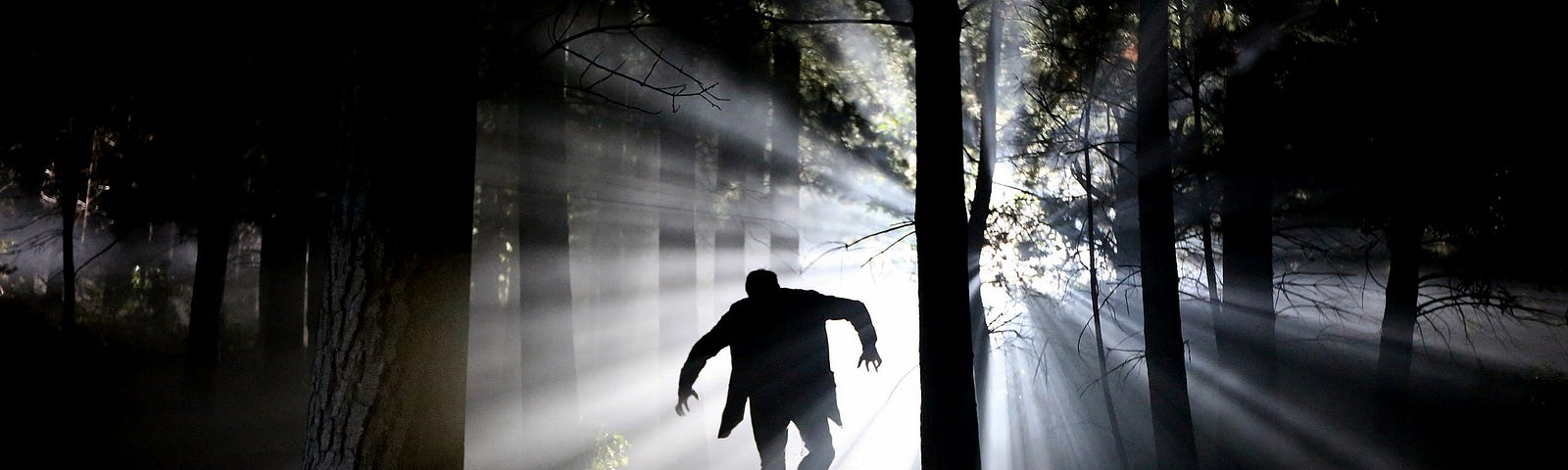 A man walks like Frankenstein’s monster through a dark forest.