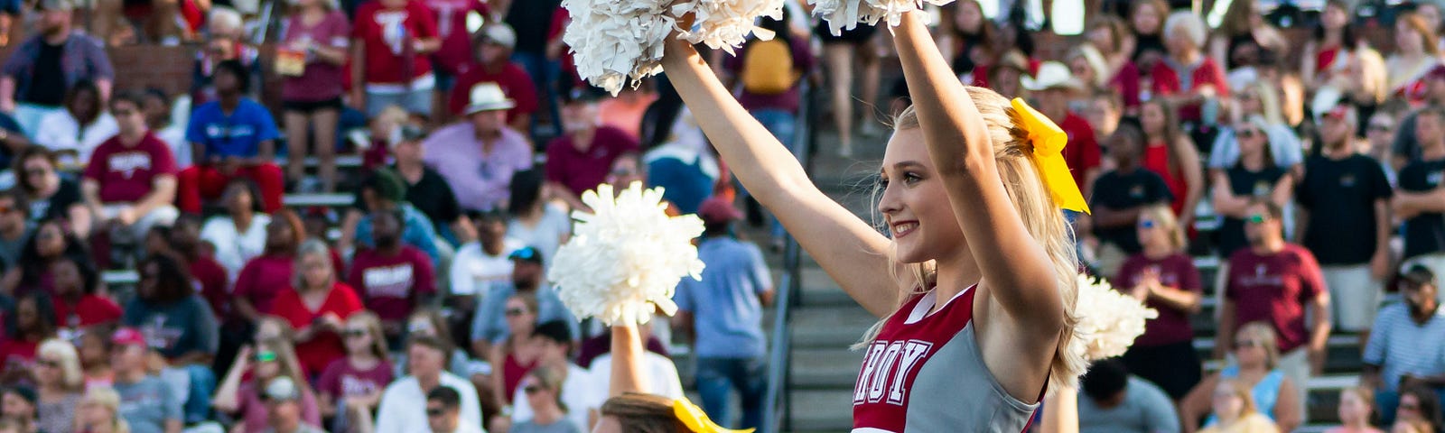 Cheerleaders with white pompoms in front of bleachers