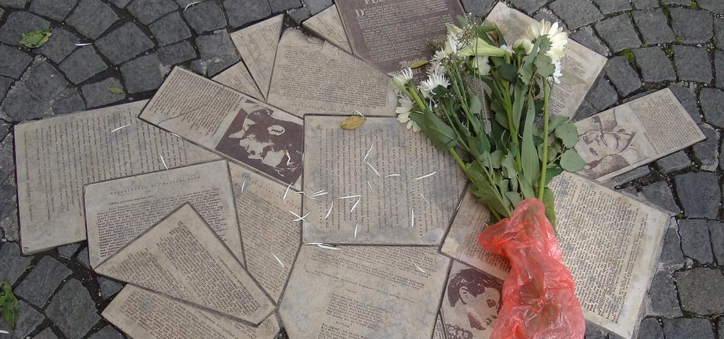 Images of anti-fascist flyers embedded into the pavement. Next to them, a bushel of white flowers has been laid down.