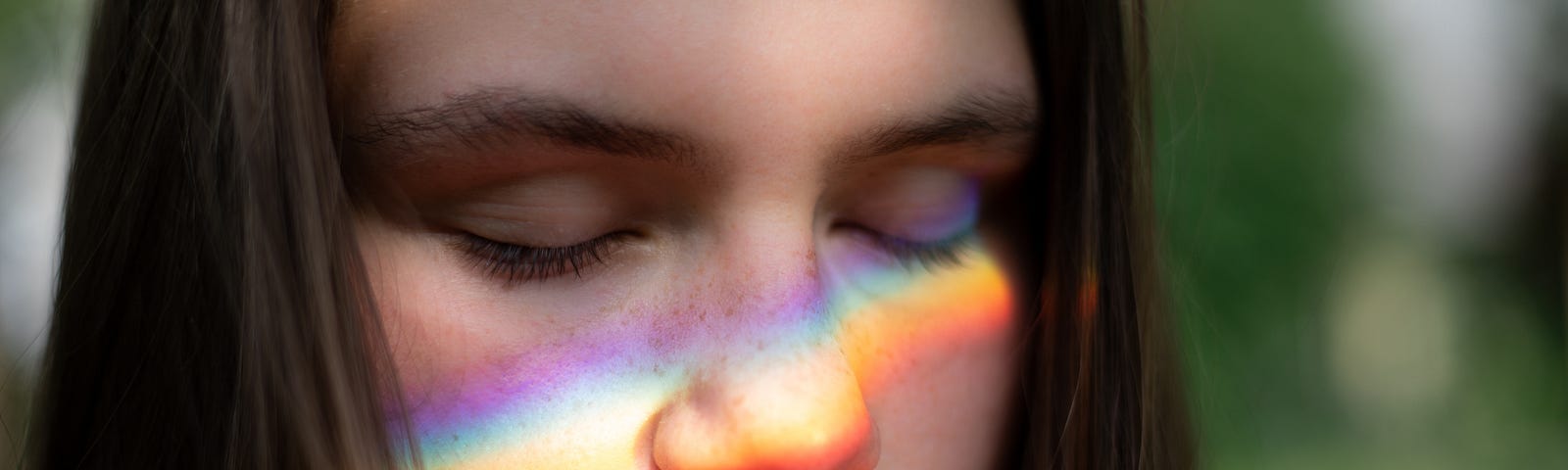 Girl smelling a pink rose with a rainbow reflecting on her face to describe an active mindfulness practice in times of Covid-19 pandemic and depression.