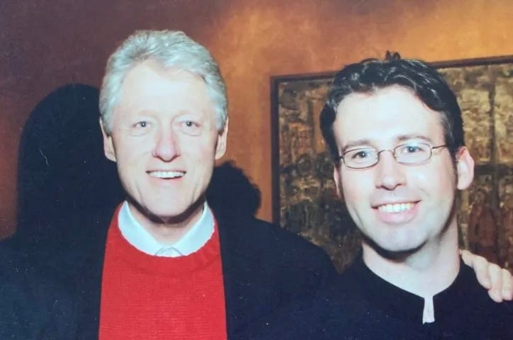 Former president Bill Clinton stands next to a young man with glasses