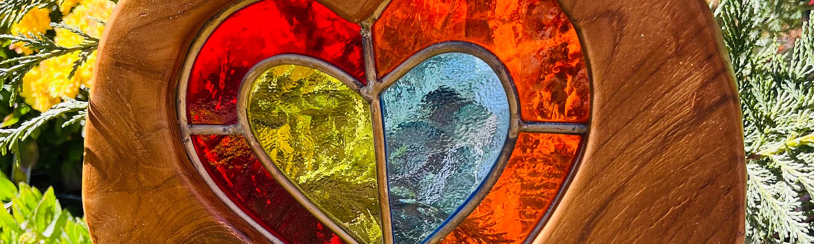A stained glass heart shines through a circular wooden art piece
