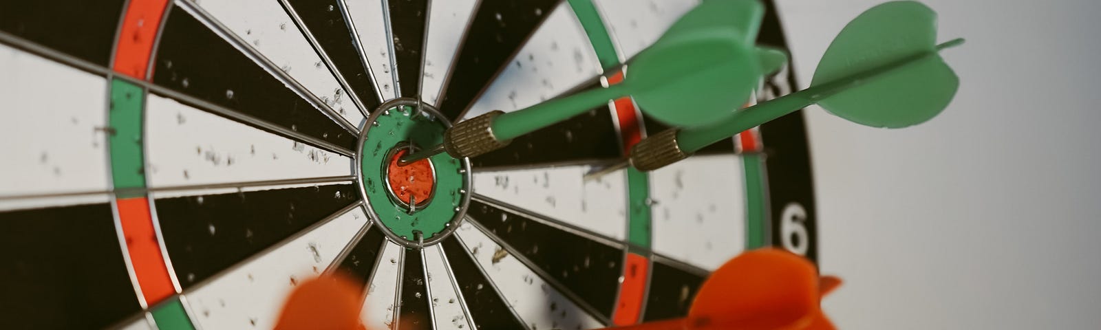 Green and red darts stuck in a red-white-black round dartboard