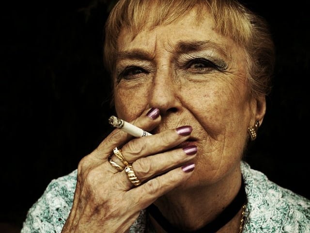 Woman with wrinkles and rings smoking cigarette.