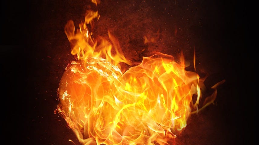 A lit candle and the resulting flame is in the shape of a fiery heart.