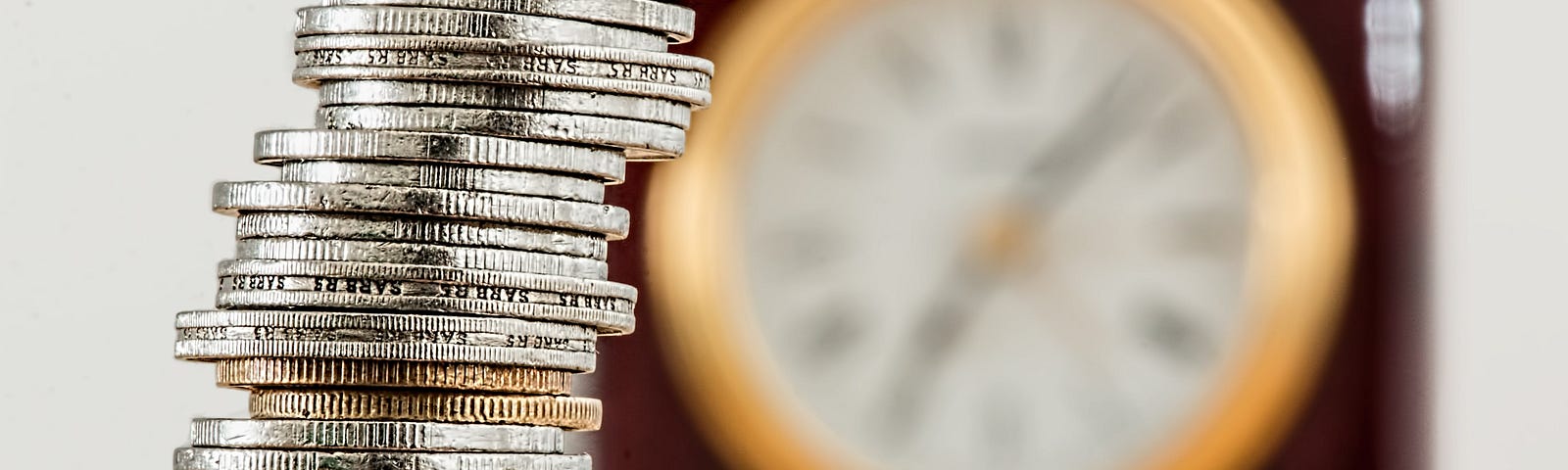A pile of coins in front of an out of focus clock