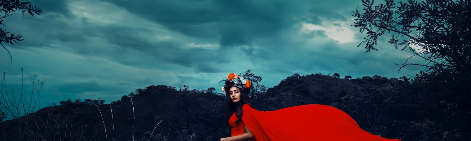 A woman in a red dress and scarf with floral headband stands amid a storm.