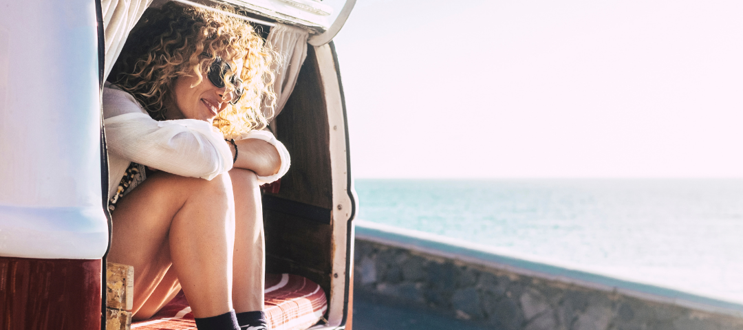 Girl sitting in the back of a camper van looking out over the ocean