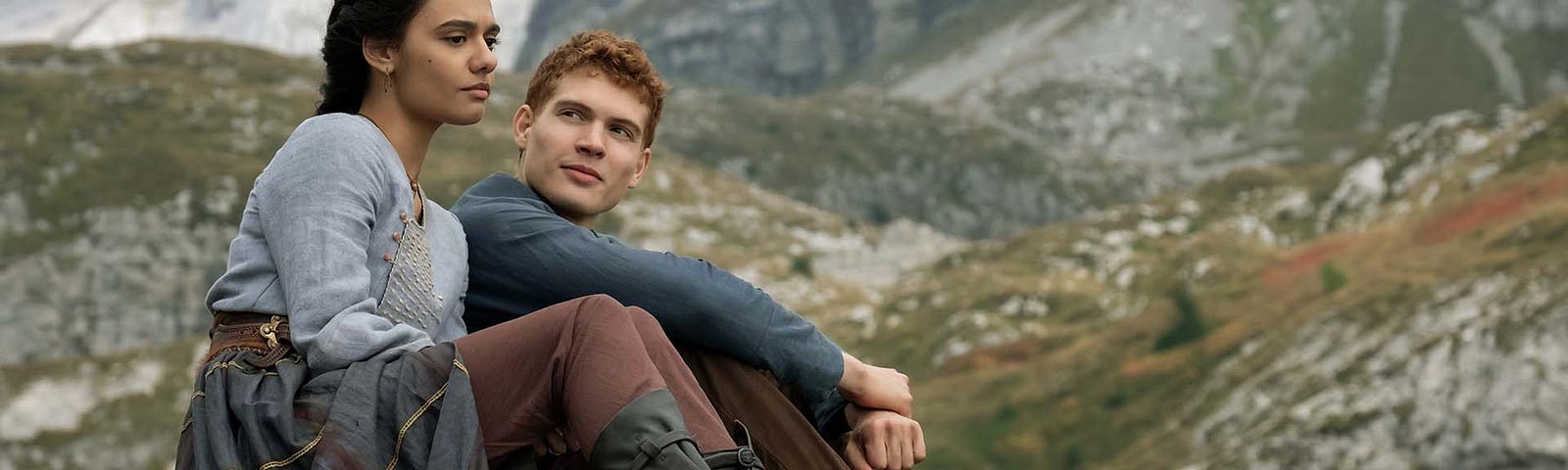 Rand and Egwene from The Wheel of Time TV show sitting together on a hillside.