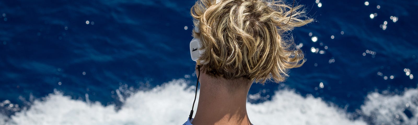 Man with headphones looking into the waves during a windy day