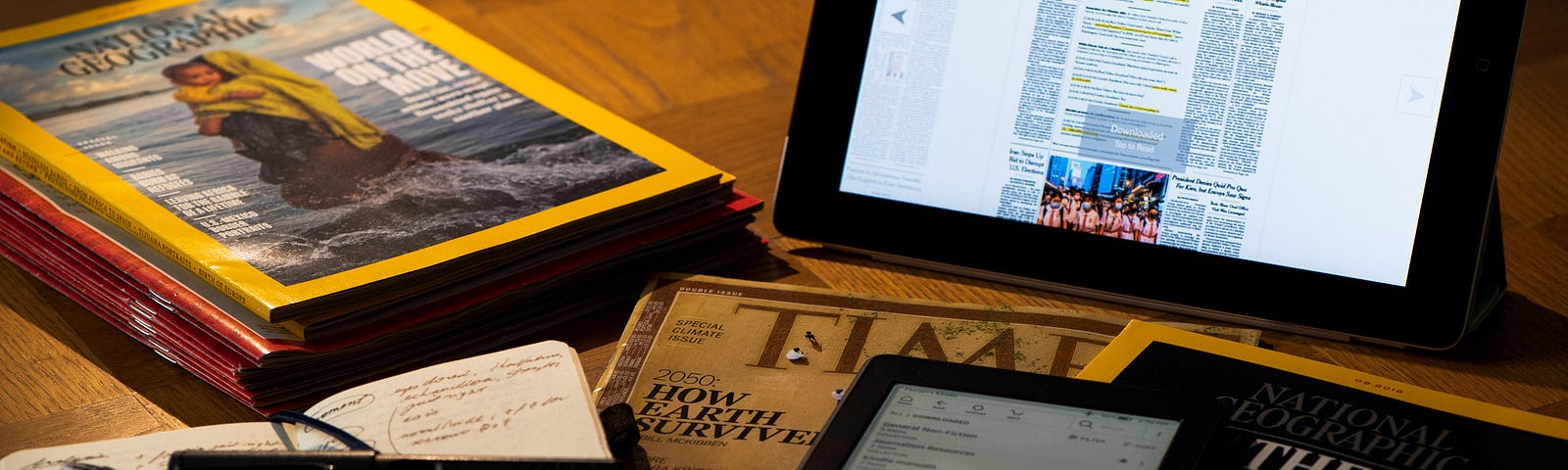 Display of magazines and newspapers, in print and digital, along with a Kindle and a pocket notebook and pens on a desk. | © Florian Schoppmeier