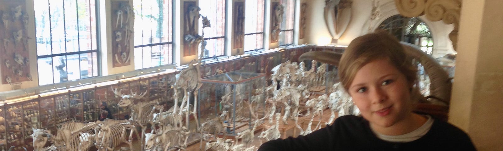 A girl stands on a walkway overlooking a room full of animal skeletons.