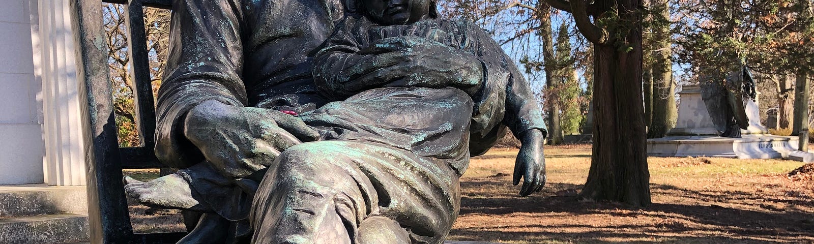 Statue of a man sitting in a chair holding a young child on his lap, his head bowed