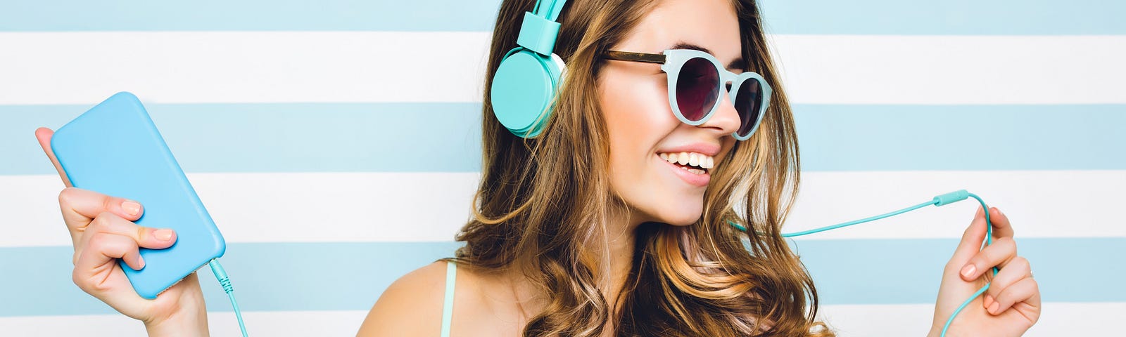 Young woman with sunglasses and headphones is dancing to music.