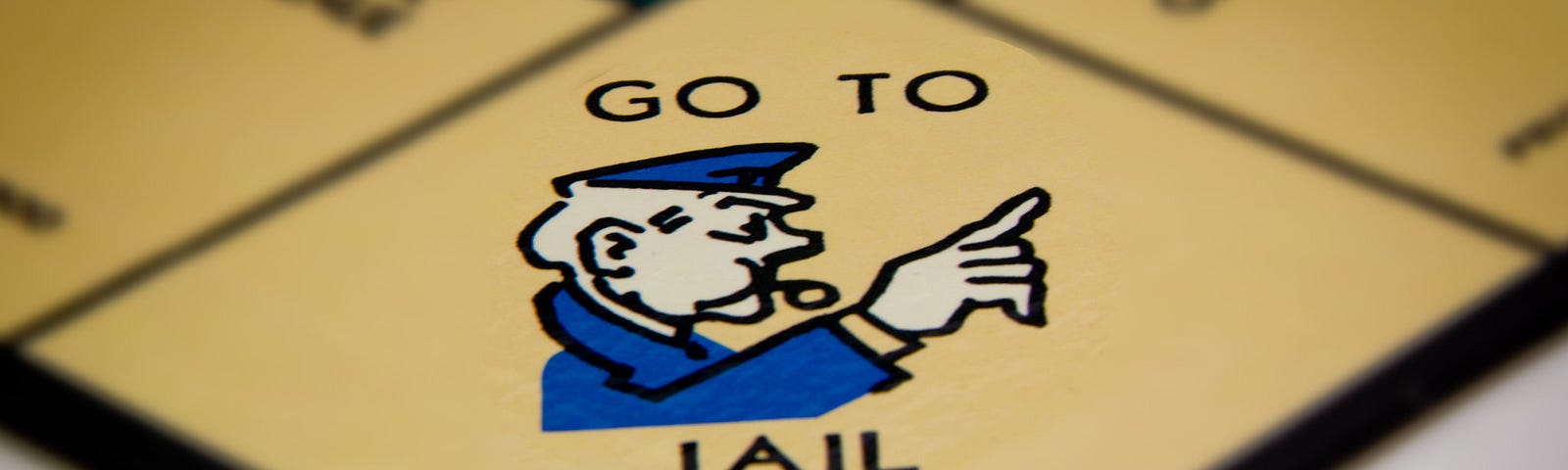 go to jail corner of a monopoly game with a cartoon police officer pointing and blowing a whistle & words ‘go to jail’