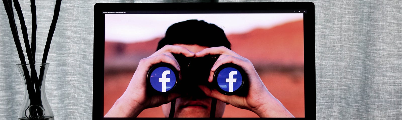 Computer screen with man looking through binoculars at you. The binoculars have Facebook’s logo on the lens pieces as if to suggest Facebook is watching you.