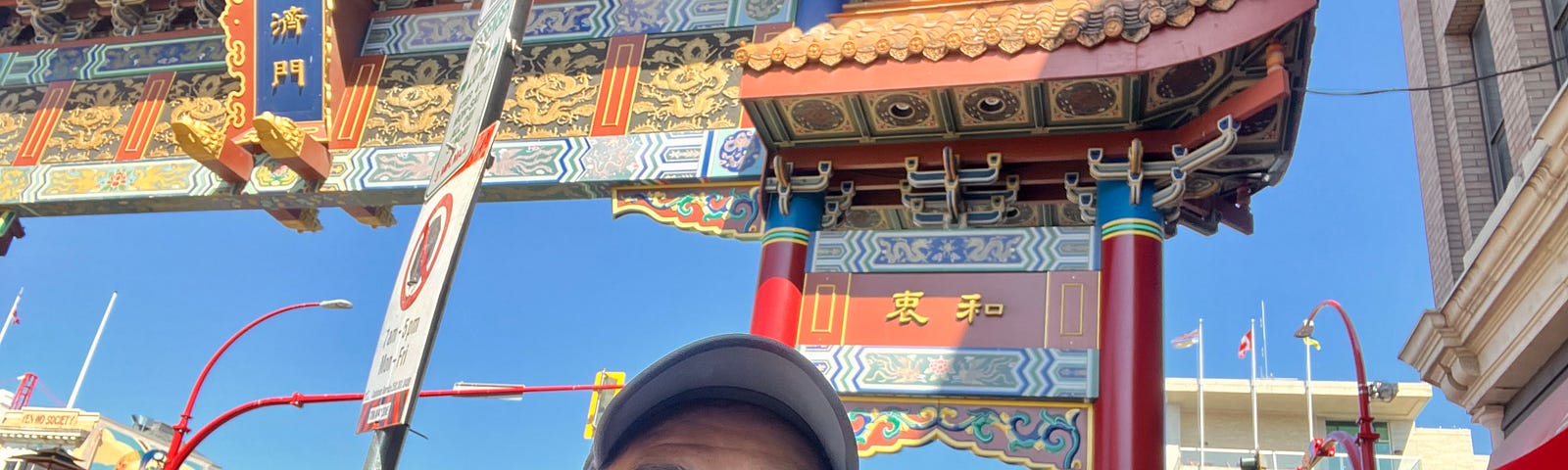 The author and his wife smiling and posing in front of the colorful gateway to the Victoria Chinatown.