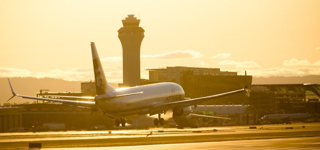 Photo of a passenger aeroplane landing at an airport at sunset, tinting the scene in warm light