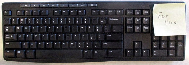 Computer keyboard with yellow Post-it Note with text “For Hire”