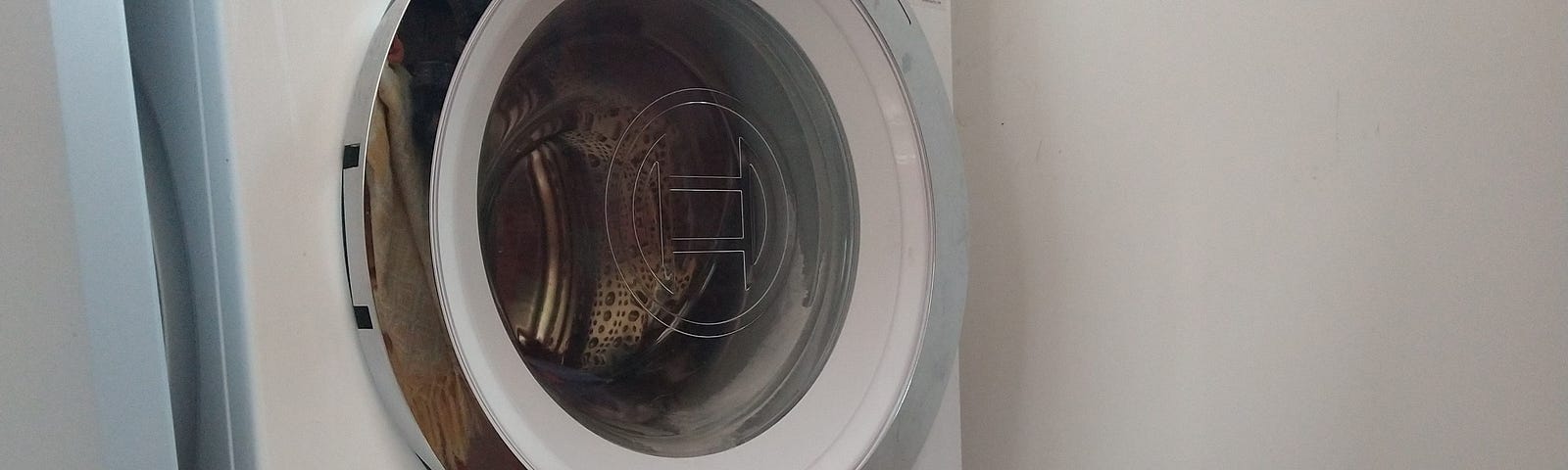 A photograph of our Bosch Washing machine, wet towel on the floor, oven tray on top of it to catch the water as it was drained.