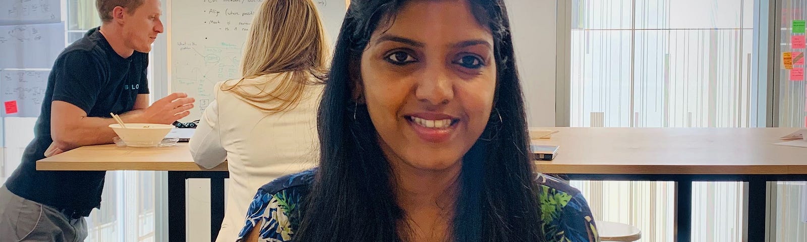 Preethi smiles facing forward while sitting in a co-working area.