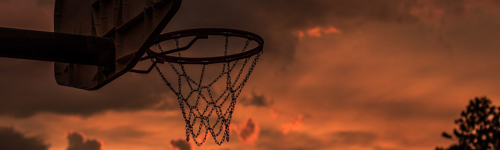 An outdoor basketball hoop shown with the sun setting.