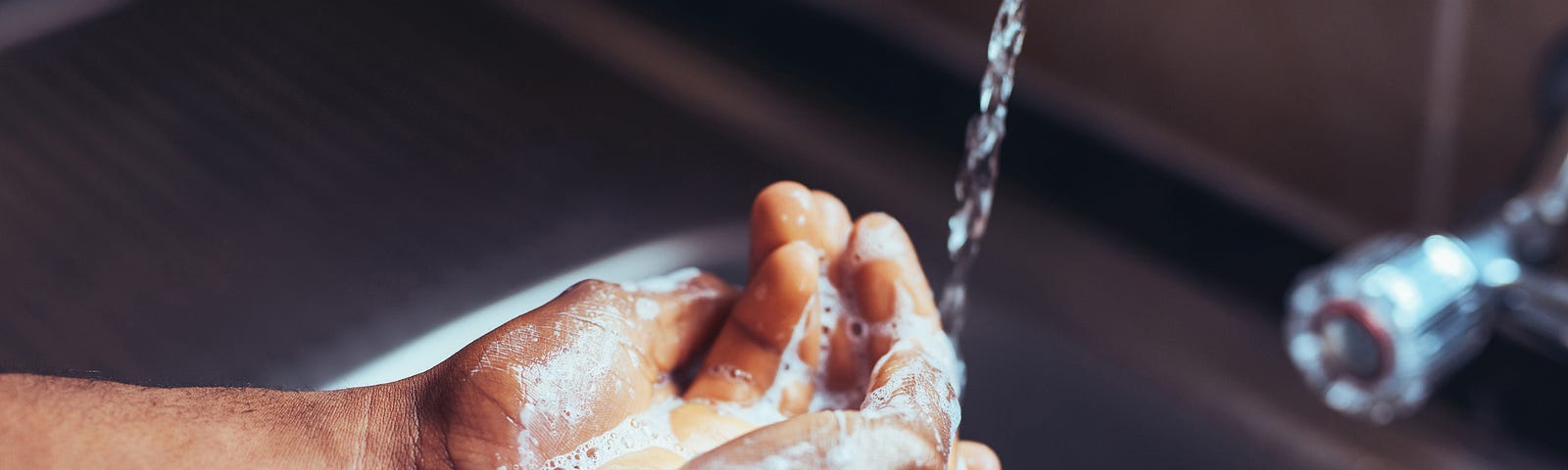 Close up of person washing their hands under sink faucet.