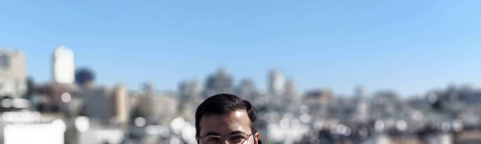 Shreyas stands smiling in front of a city skyline.