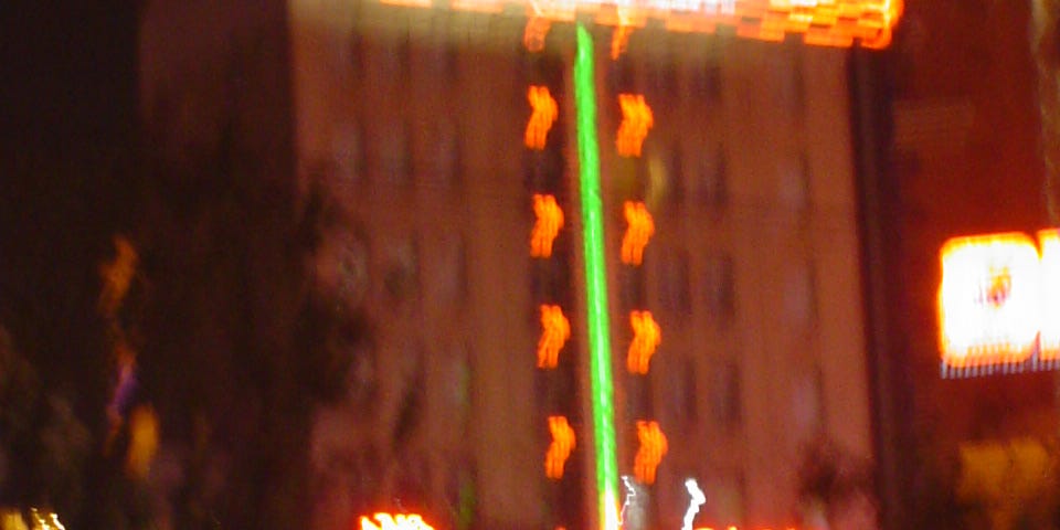 A shaking out-focus night time snapshot of an orange & green neon sign thermometer on the exterior of a building in Shanghai.