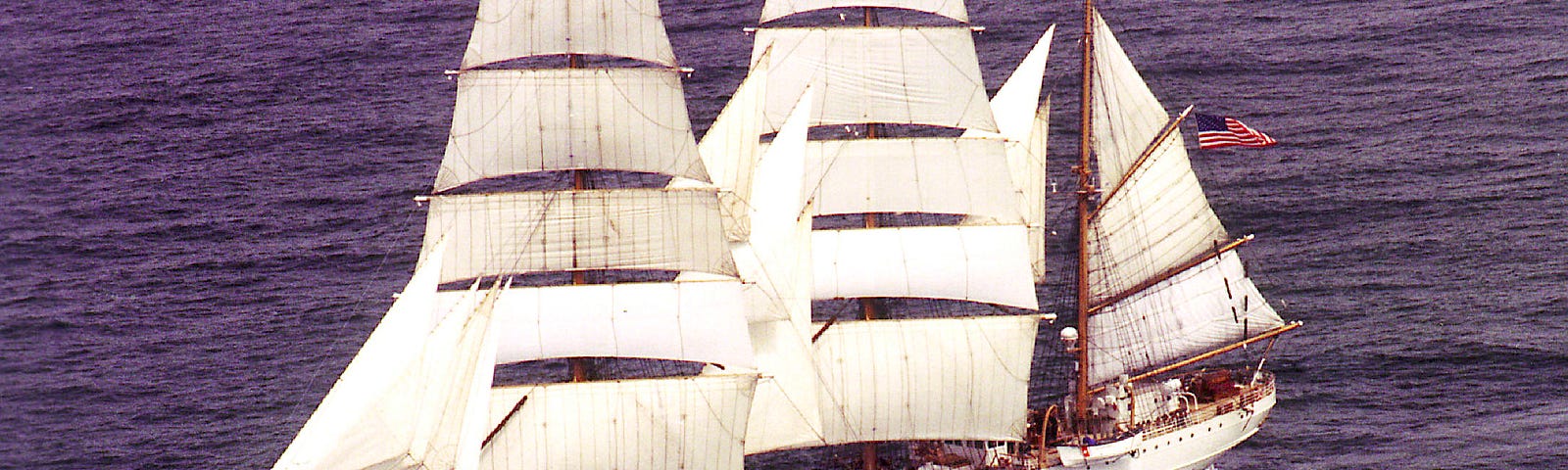A large three-masted U.S. Coast Guard sailing ship is under full sail on the high seas.