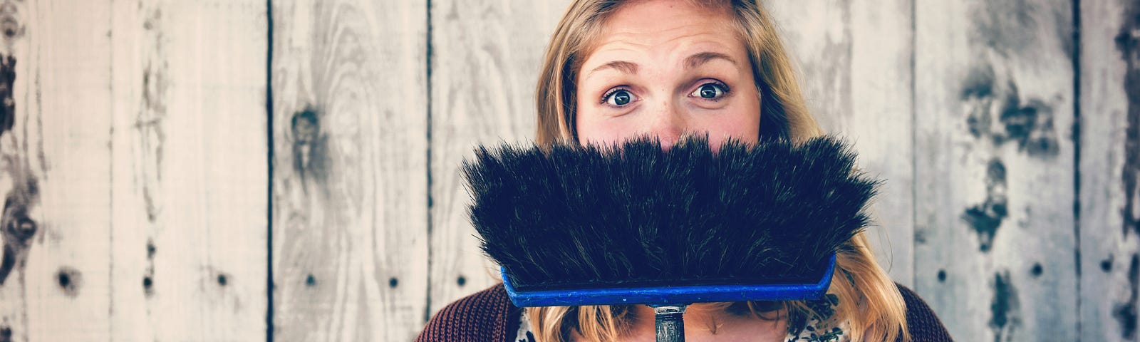 A lady smiling behind a broom.