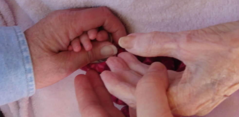 Photo of four generations of hands holding together. A baby’s hand, mom’s, grandma’s, and great grandma’s.