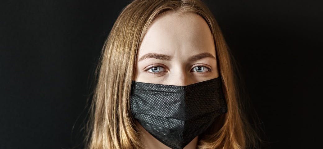 A woman in black wears a black face mask against a black background. emotional contagion.