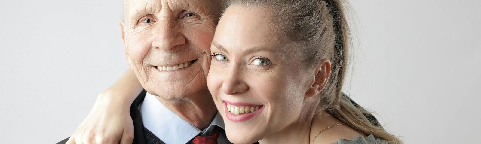 An attractive young woman has her arm around the shoulders of a well-dressed elderly man and both are smiling.