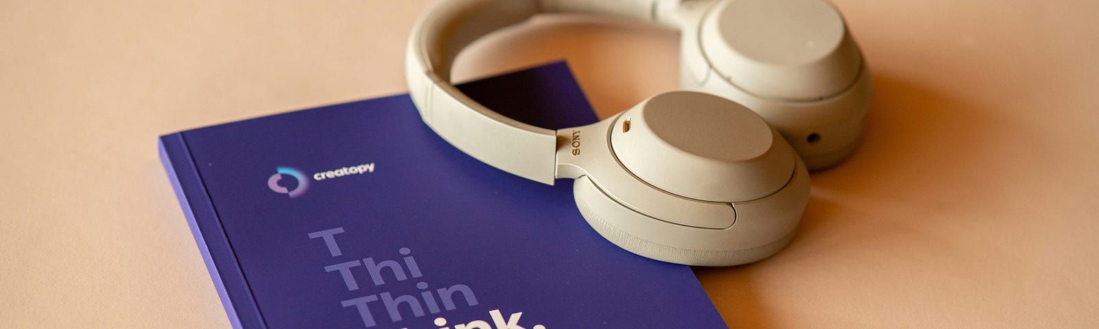 Notebook with “think” on it and headphones on a minimalist office desk.
