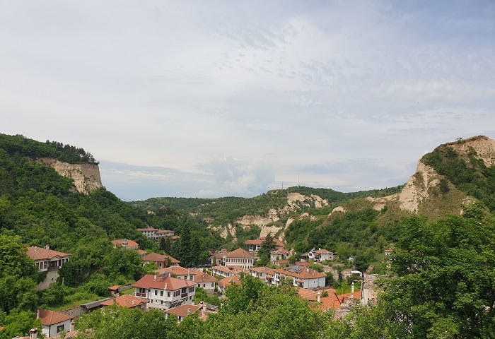 small bulgarian town of white houses with orange roofs surrounded by sandy and craggy hills and green trees