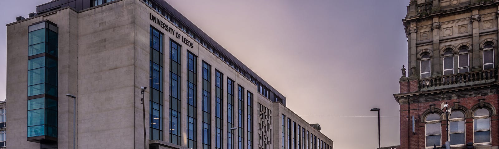The University of Leeds School of Chemical Engineering Building at sunset, with pedestrians crossing the street next to The Library pub.
