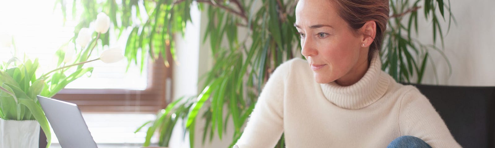 A woman writing on a note pad while looking at her laptop.