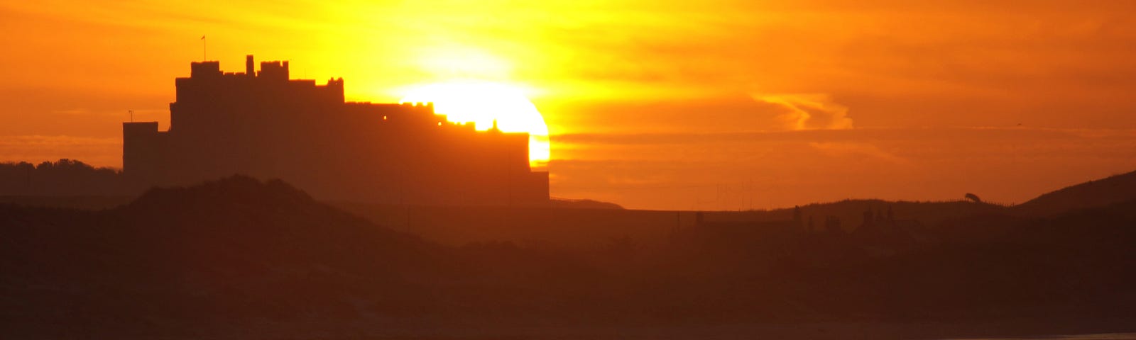 The sun sets behind Bamburgh Castle colouring the sky and sea in brilliant hues of yellow and orange