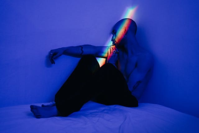male in black pants sitting on bed. Picture through blue lens