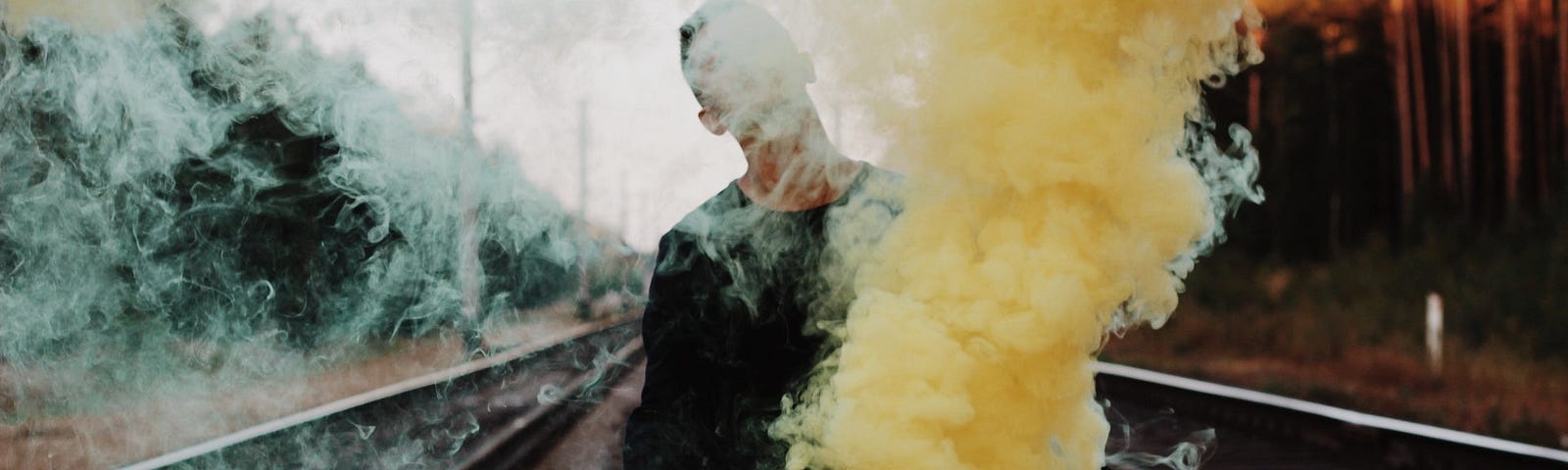 Man standing between train tracks holding yellow smoke bomb