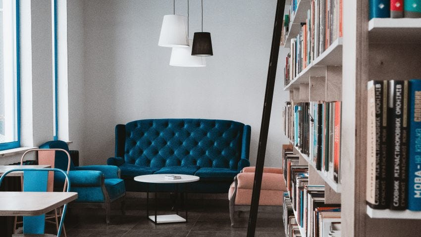 tufted blue couch in library. shelf of books on the right with ladder. concrete floor.