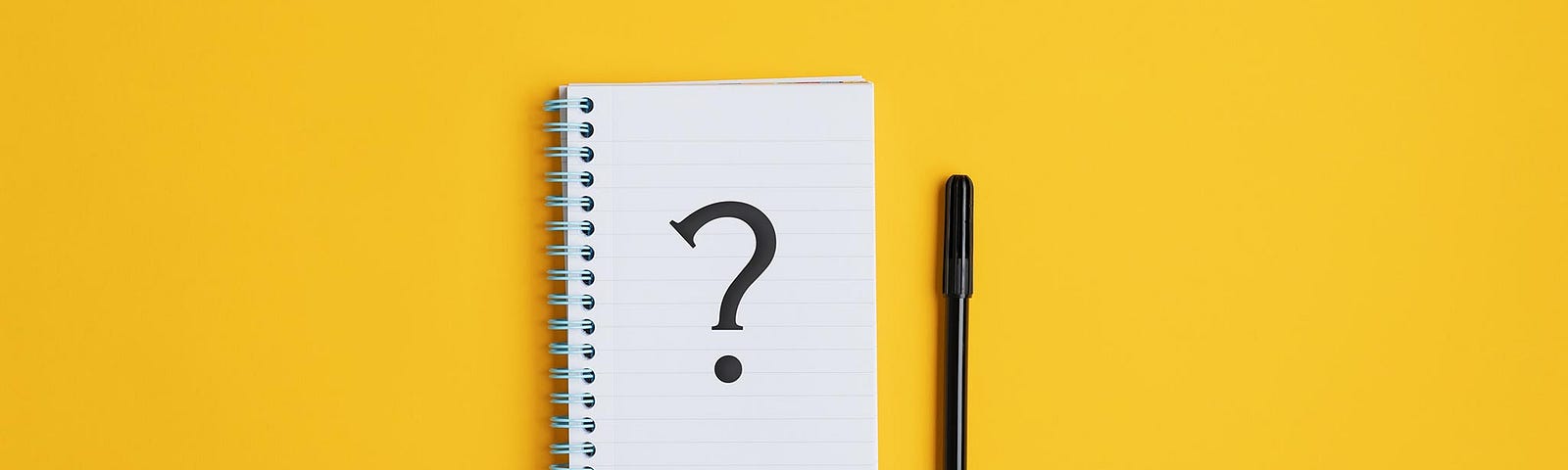 A notepad with a question mark drawn on it. Next to it is a pen. The background is a bright mustard yellow.