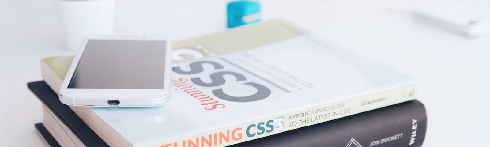 Stack of books on a desk with a phone on top of it, Javascript and JQuery on the bottom and Stunning CSS on top.