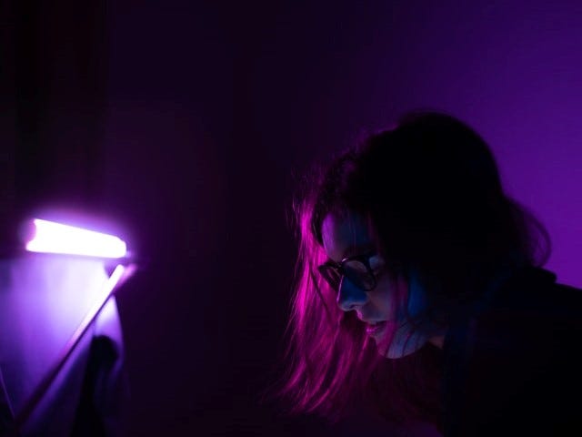 A person looking at a phone in a purple lighted room