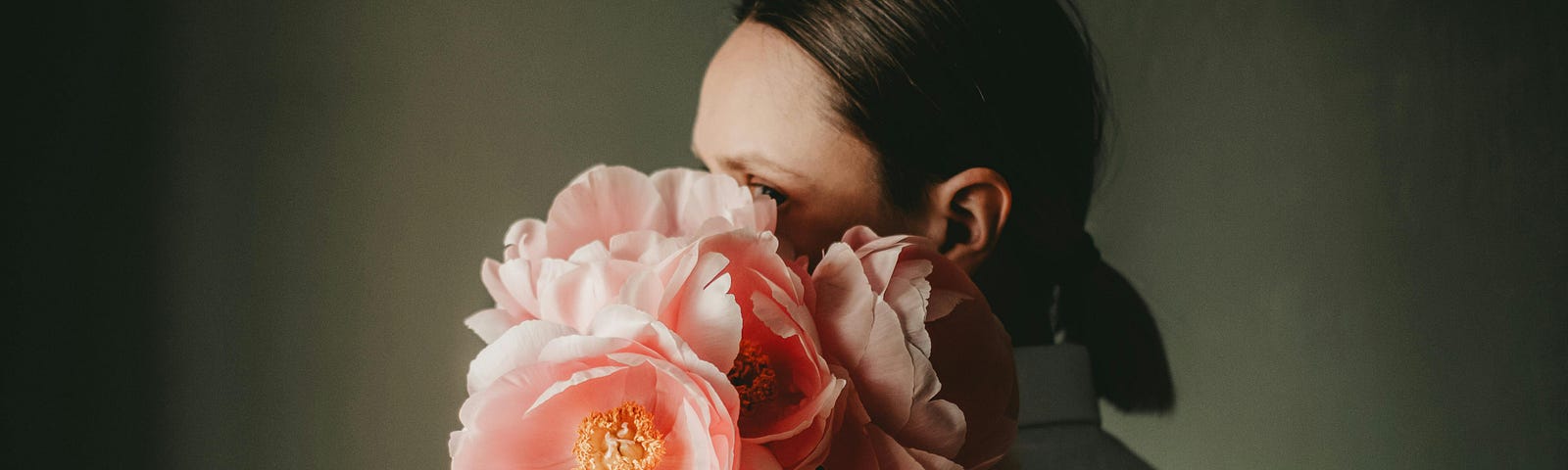 A woman with her face obscured by a bouquet of pink peonies.